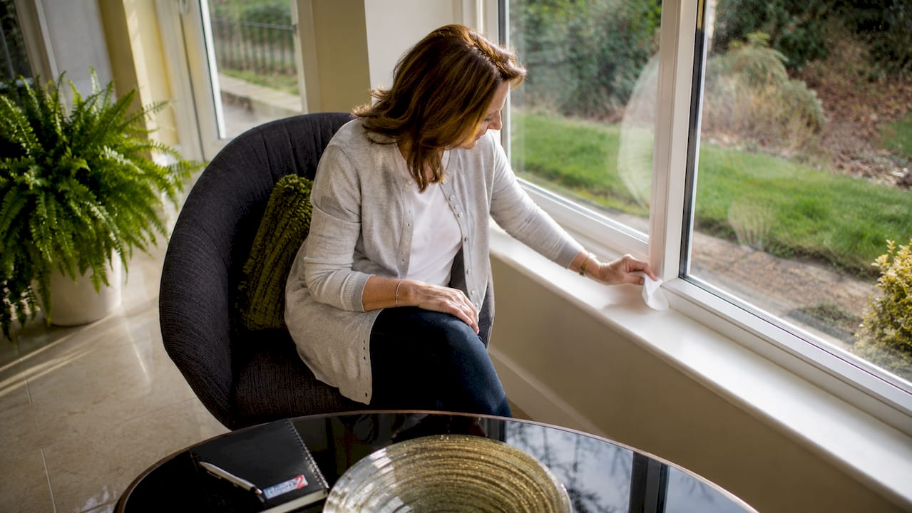 Woman testing window draught with tissue near window frame