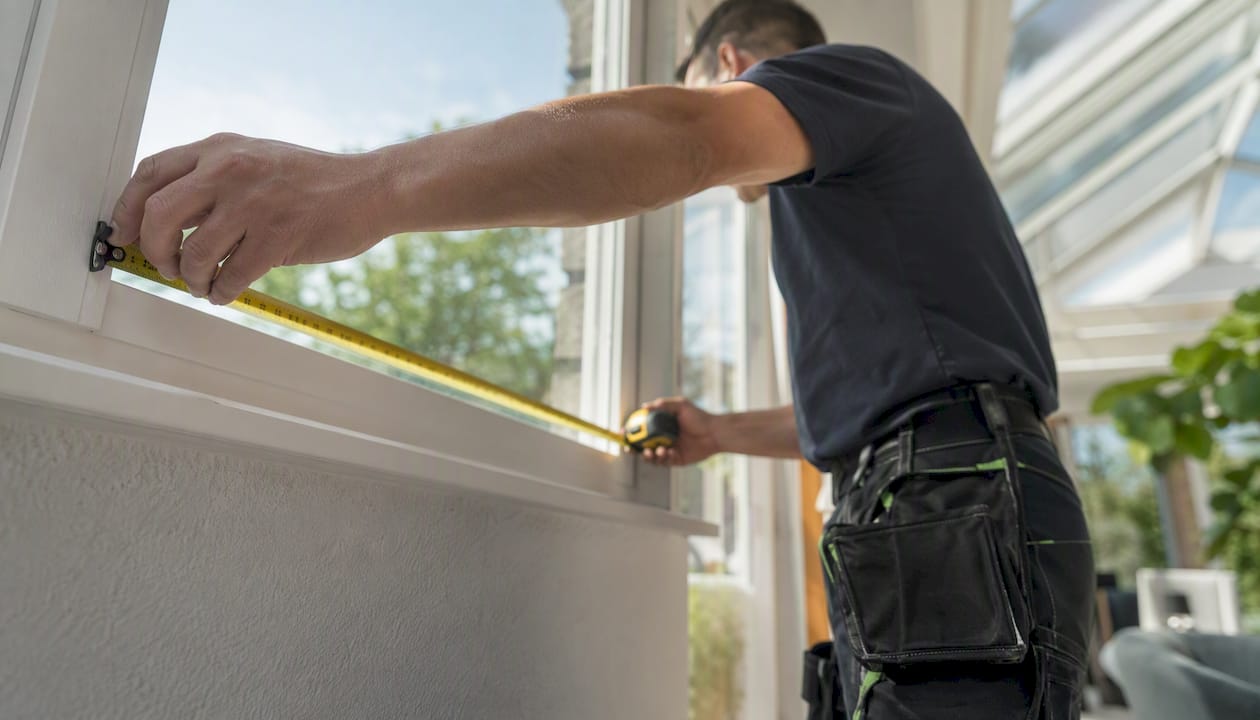 Hands measuring window frame indoors